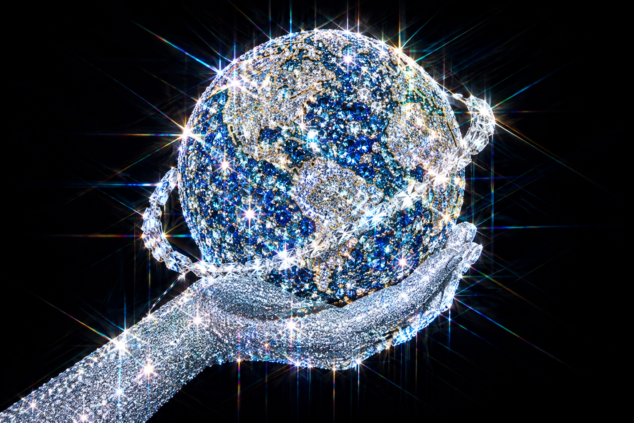 A jewel-covered hand holds a blue and silver jeweled Earth with a sparkling orbital ring against black.