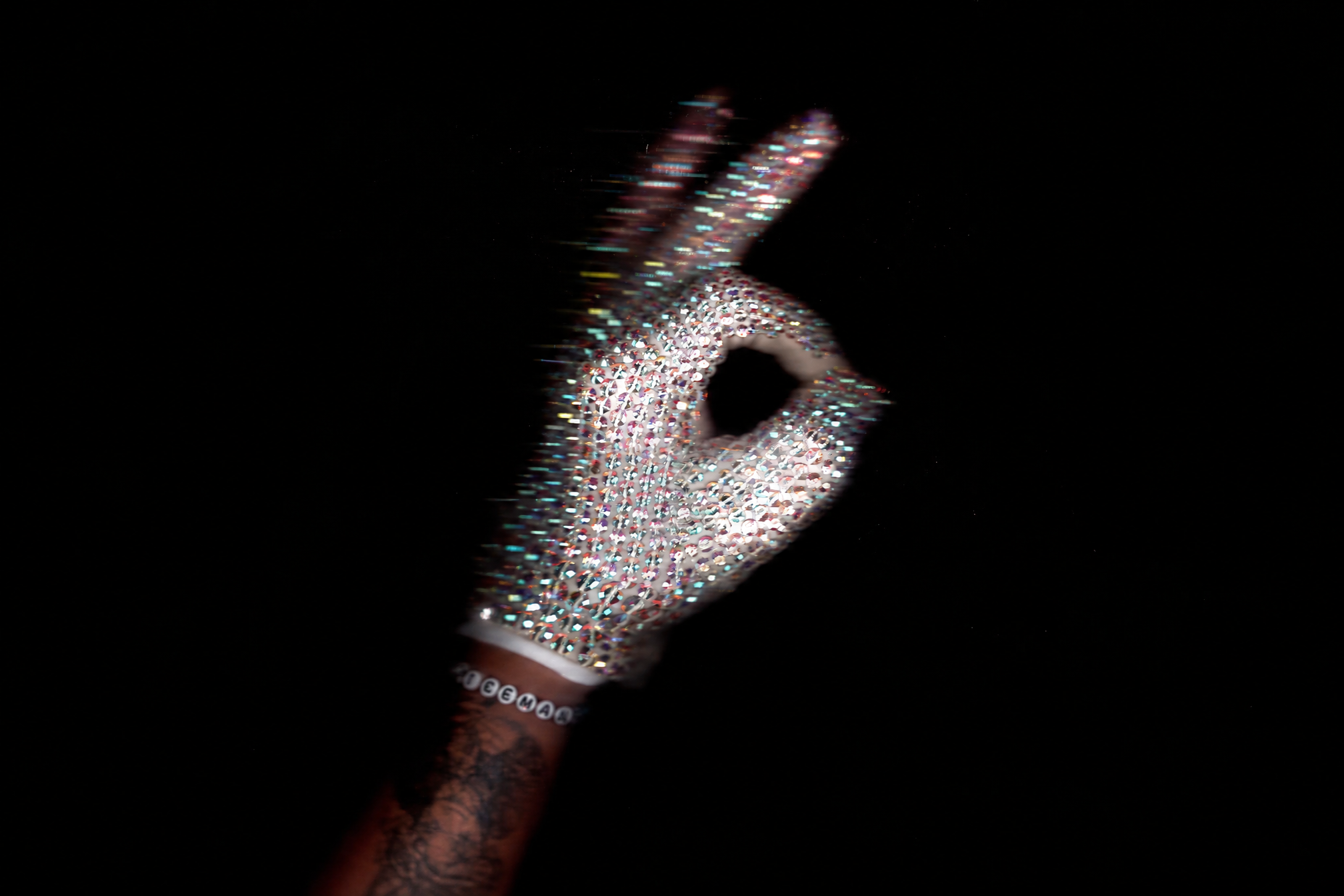A rhinestone-covered glove forms a circle with thumb and finger, with motion trails against black.